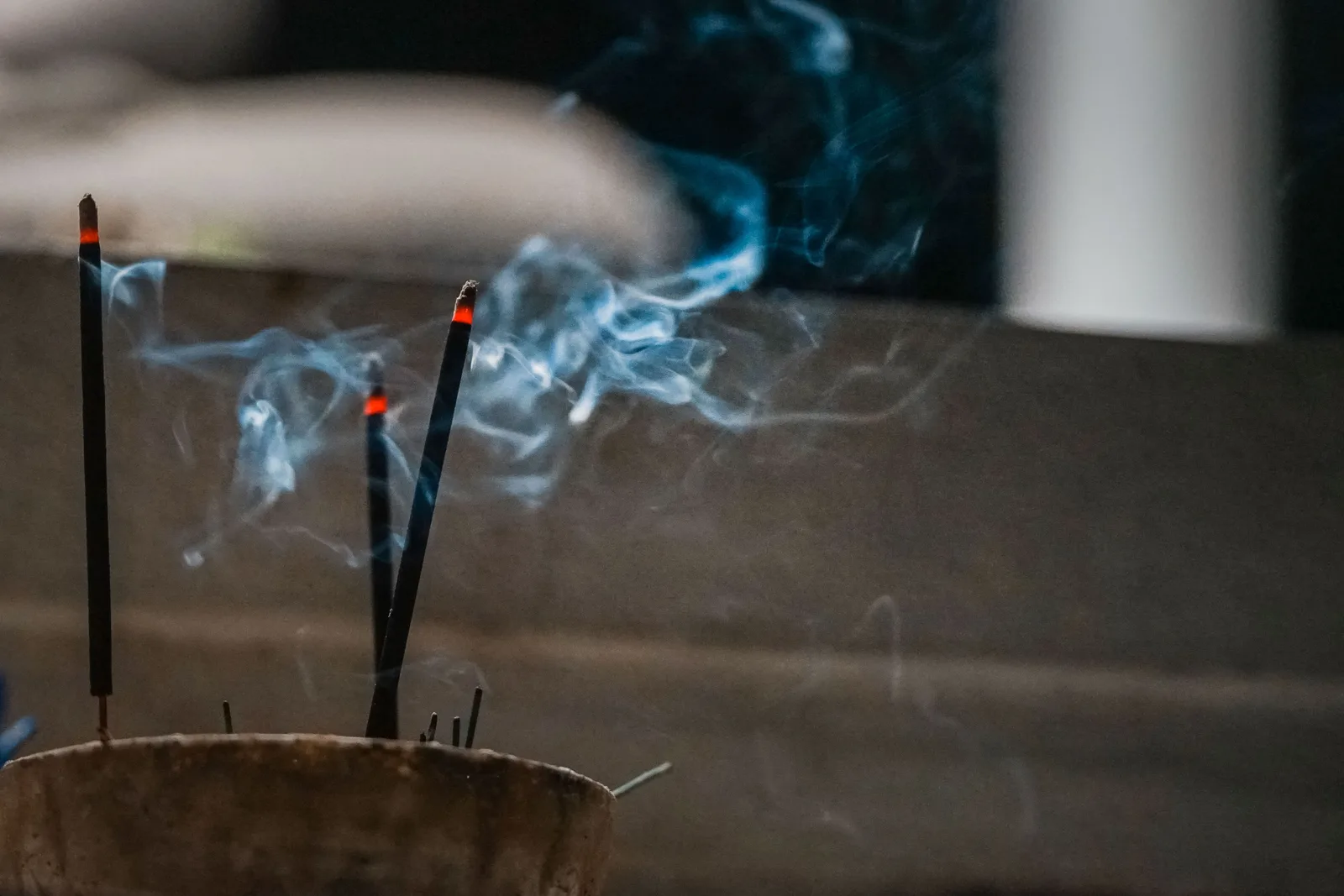 Des bâtons d'encens allumés, volutes de fumée dans une lumière douce