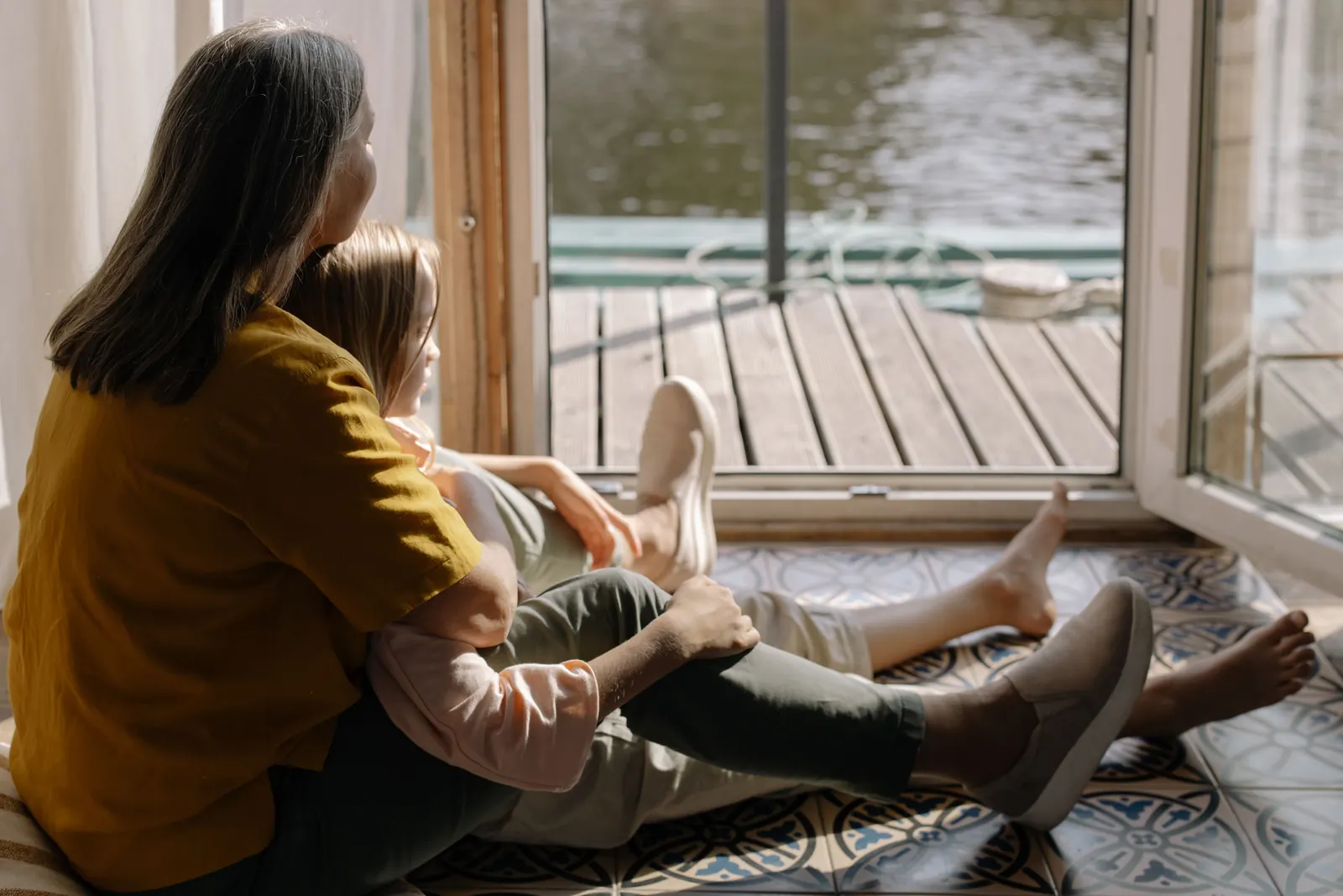 Une mère et sa fille assises devant une fenêtre, la transmission silencieuse d'un rôle de génération en génération