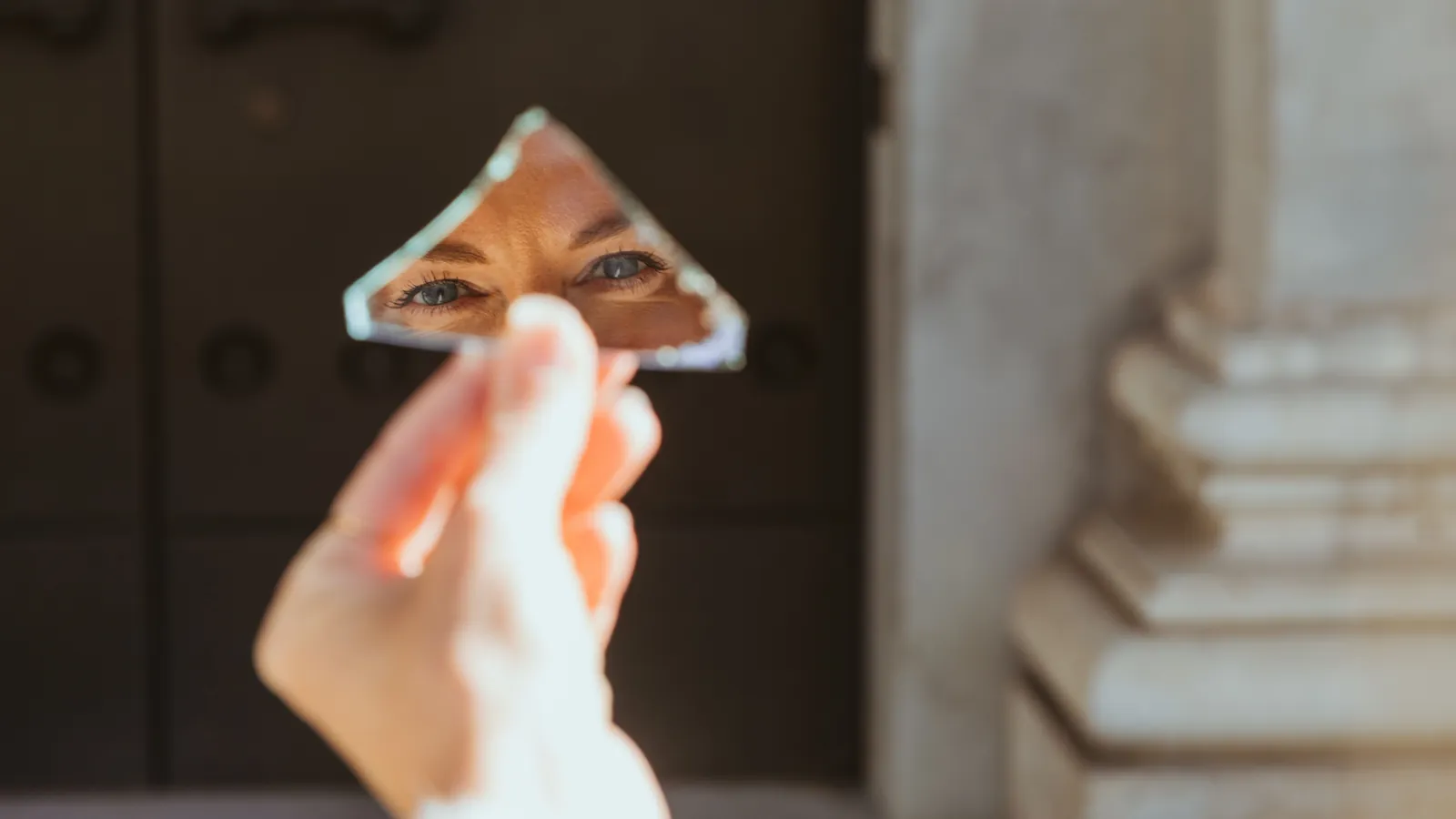 Une personne se regarde dans un éclat de miroir brisé tenu à la main